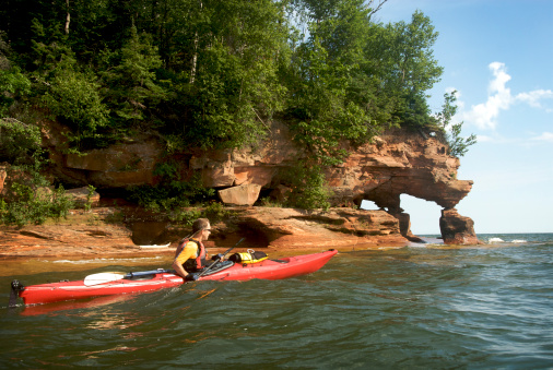 57-year-old man paddling a 16.5-foot sea kayak along the shore of Sand Island, one of the Apostle Islands off the shore of Wisconsin in Lake Superior. The rock formation is one variation of \