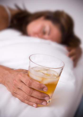 Alcoholic woman sleeping and drunk with a glass of Whisky in the Bed