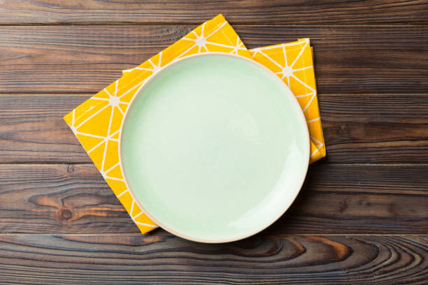 色付きの背景に上面図、食べ物用のテーブルクロスに空の丸い緑のプレート。あなたのデザインのためのスペースを持つナプキンの空の皿