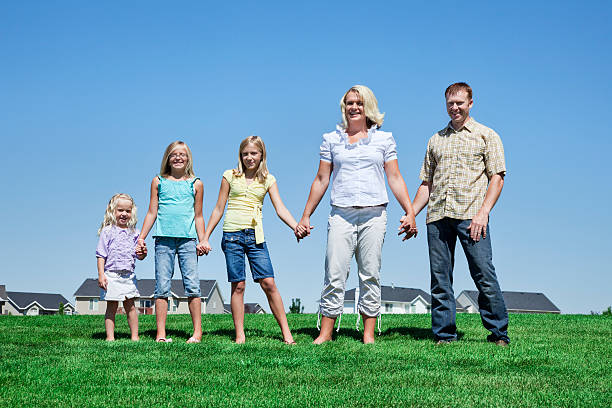 Family of Five Holding Hands in Neighborhood Park Photo of a young family of five in a neighborhood park, holding hands as they stand side by side. mormonism stock pictures, royalty-free photos & images