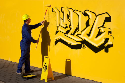 Young man spray painting colorful graffiti on a clean orange wall