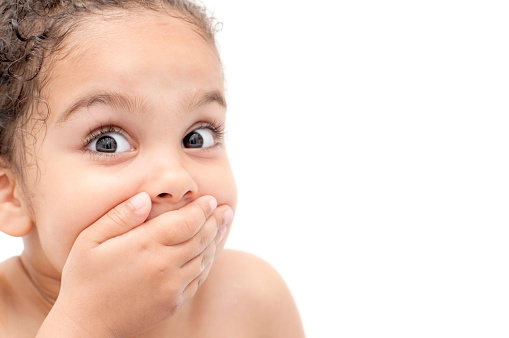 Royalty free stock photo of 4 years old girl with her hand covering her mouth. 