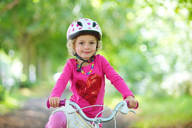 Toddler is doing thumbs up gesture and is wearing a pink helmet and wrist protection and is looking at camera on pure white background. She is about to learn skating.