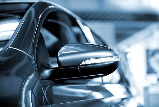 A close-up, centered picture of the left-hand side mirror of a new dark blue car.  Light is visible on the highly reflective body of the car.