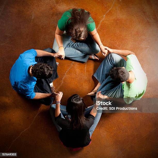 Group Of Young Adults Holding Hands And Praying Together Stock Photo - Download Image Now