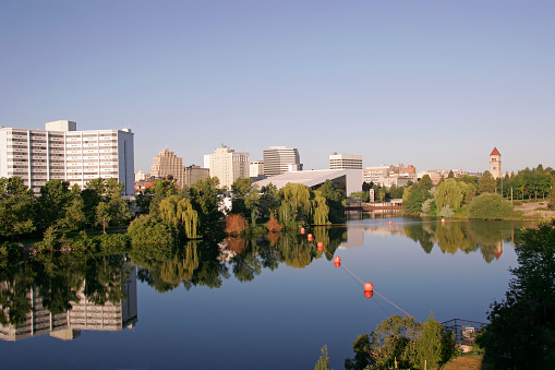 Spokane River and Riverfront Park with beautiful early morning reflections.. Lined with wispy willow trees at water's edge. Perfoming Arts Center and Clock Tower in park. Heritage buildings in background.