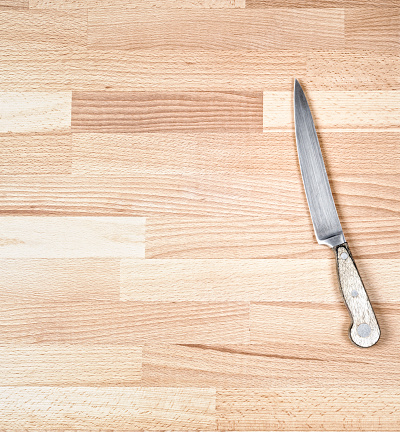 A wooden handled kitchen knife on a large chopping board surface.