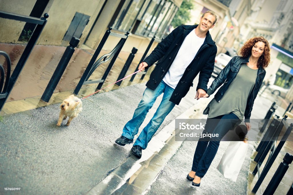 Couple shopping and walking under the rain Cross-processed image of a middle age couple walking under the rain. Street shopping with a bag paper in the city. Dog Stock Photo