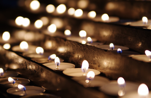 Candles in a raw with shallow depth of field, with light glow of other candles in the background