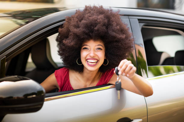 istock Smiling young woman showing car key while sitting in car 1576504130