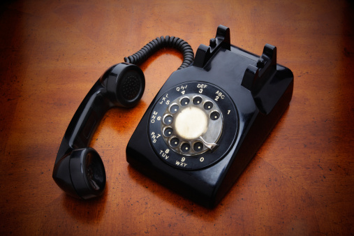 A black rotary phone, with the receiver off the hook.