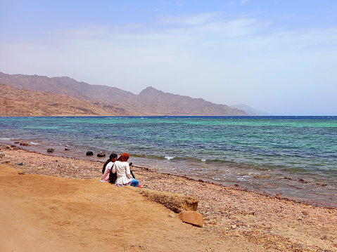 May 2023, Dahab, Egypt: Bedouin girls sitting looking at the sea on the shores of the Red Sea in the Sinai Peninsula. Religions and Berber culture of the Arabian desert.