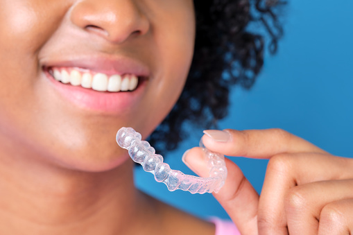 closeup of unrecognizable african american girl smiling with transparent dental retainer in hand on blue background
