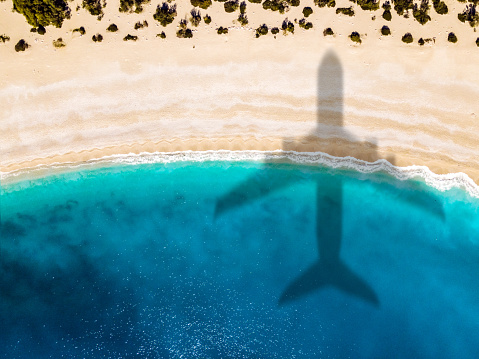 Vacation at tropical paradise near sea. Aerial view of beach and sea shore with airplane arriving at destination. Summer vacation background with place for text. Shoot directly above.
