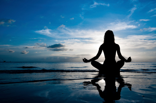 Silhouette of woman in lotus position sitting in sea and medditating