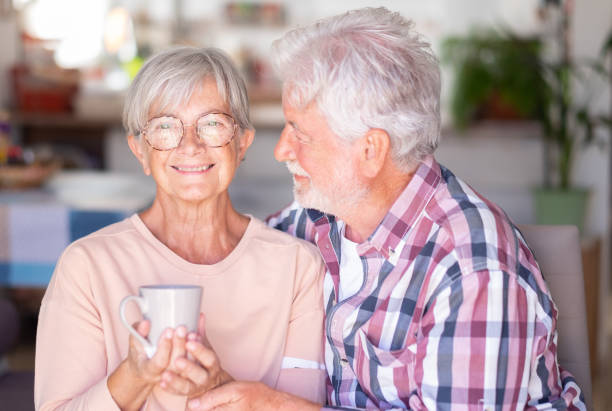 istock Senior white-haired man embracing and looking with affection at his wife drinking a cup of coffee or tea. Forever love, elderly couple in love 1576573817
