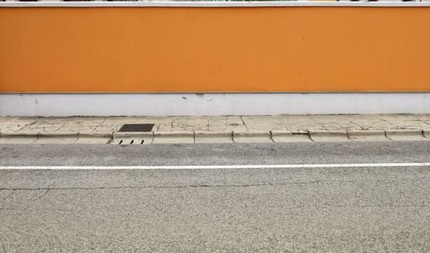 istock Orange and white plaster surrounding wall with sidewalk and road in front. 1576606878