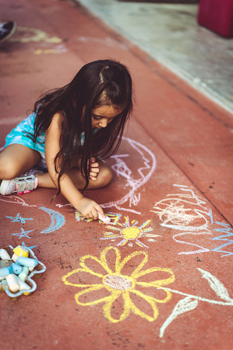 Chalk drawing rainbow colors on the asphalt, children outdoors.