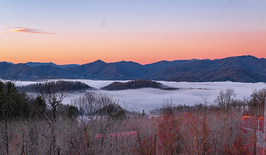 A fiery sunrise overlooks the Blue Ridge Mountains with fog islands in the French Broad River Basin