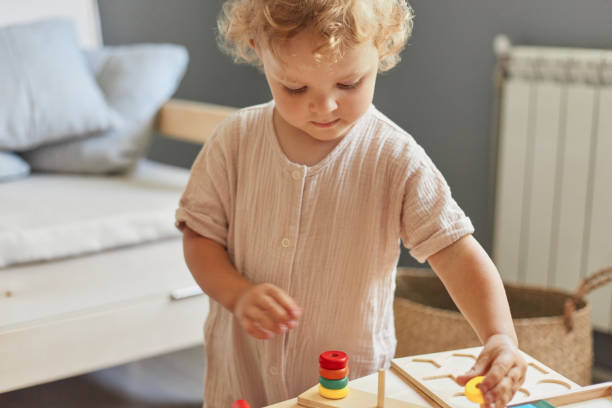 istock Cognitive development puzzles. Montessori learning approach. Wooden construction set. little blonde baby girl palying with wooden sorter toys at home interior 1576632073