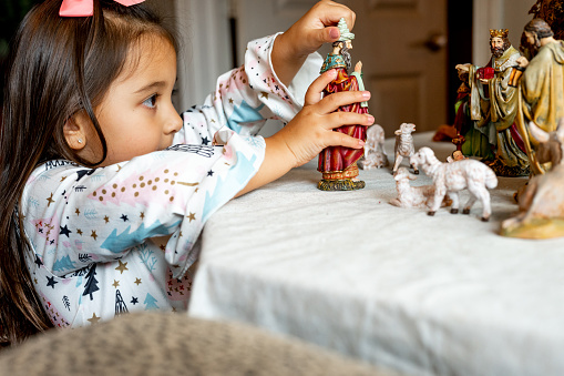 A cute young girl plays with a nativity set at home
