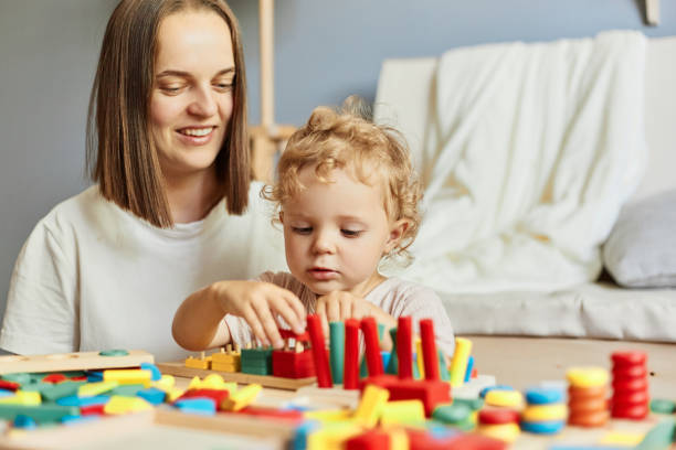 istock Fun nursery activities. Educational playroom setup. Toddler's imaginative play. Creative art sessions. Teacher or mother playing with baby with logical toys at home interior. 1576637626