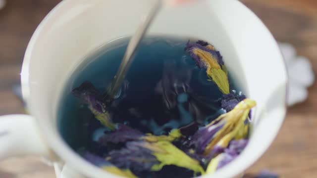 Stirring Blue Thai Anchan Butterfly pea flower tea in mug cup with teaspoon.