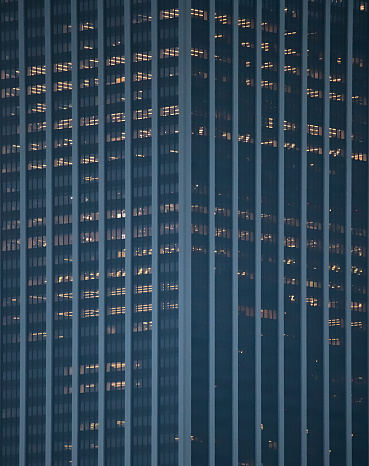 tall office building detail (straight lines, symmetry) dark with lights on in some windows (skyscraper, downtown urban tower) nyc, manhattan, new york city real estate at night