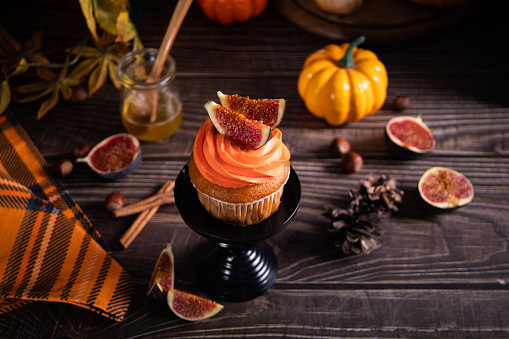 Delicious homemade autumn season spicy pumpkin cupcakes with whipped orange cream with fruit figs