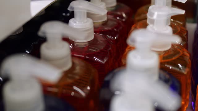 Close-up of unlabeled plastic bottles of red, blue, orange color stand in rows. Generic multicolor liquid cosmetic and body care goods in cardboard box on retail discount store shelf.