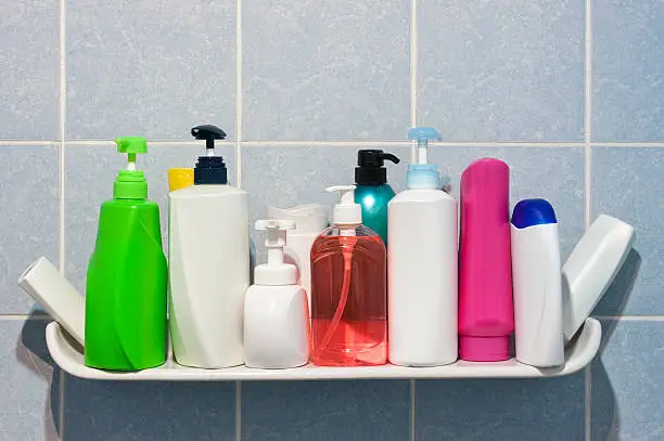 Photo of Many shampoo and soap bottles on a bathroom shelf.