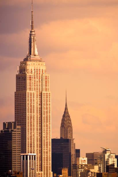 Image of the cityscape of New York City, featuring the Empire State Building and the Chrysler building, amongst other skyscrapers with the light of sunset creating a retro feel to the composition.