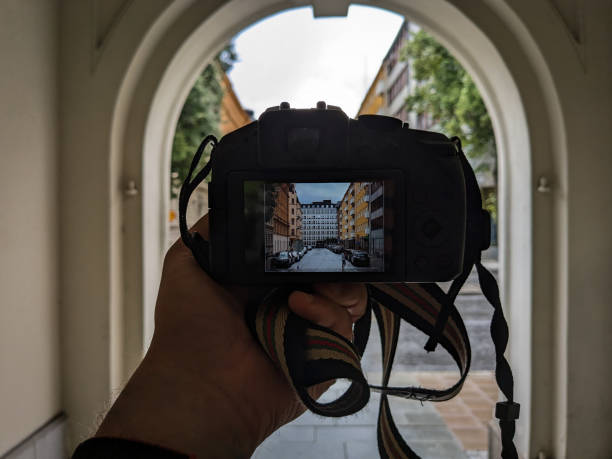 A person with a camera pauses to photograph surroundings in a residential city block. The image highlights the everyday act of exploring and documenting urban life.