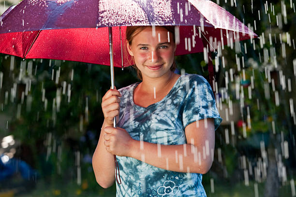 While sitting on a park bench under an umbrella, a woman reaches out to check if the rain is still falling
