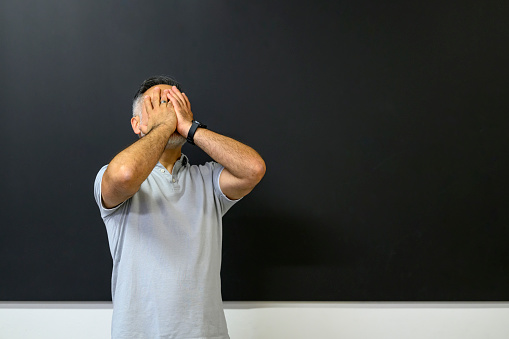 Desperate teacher with his hands on his face standing at the blackboard in a classroom