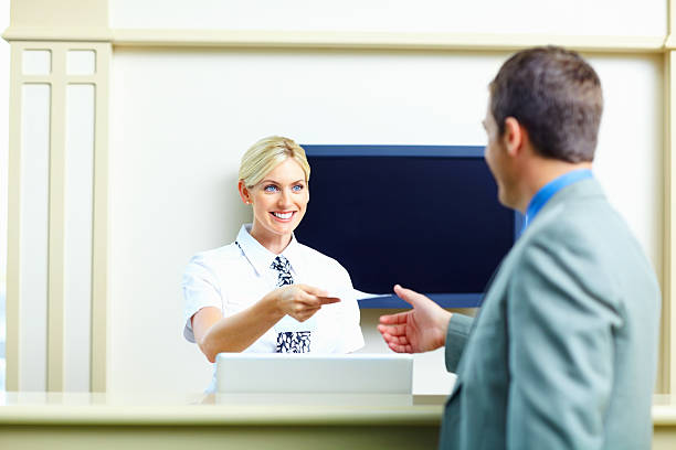 recepcionista sonriente dando un pasaje aéreo a un hombre de negocios - tv reception fotografías e imágenes de stock