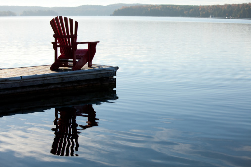 An adirondack chair by a lake. Image taken in the Muskoka region of Ontario, Canada. This region is known for being cottage country. Towns such as Gravenhurst, Deerhurst, Barrie, and the Algonquin are prime summer holiday destinations. 