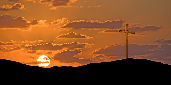 A gold colored cross under a very dramatic sky with a setting sun.