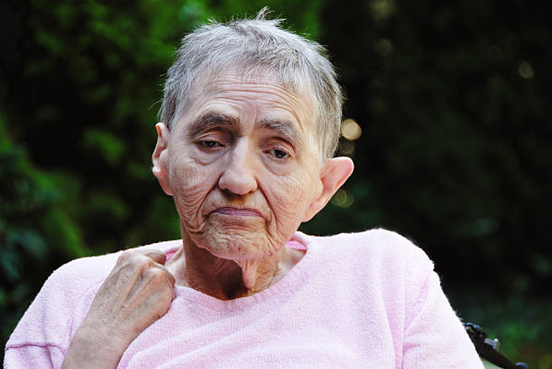 senior woman, disabled and with Alzheimer disease, sitting  in the garden on a summer day