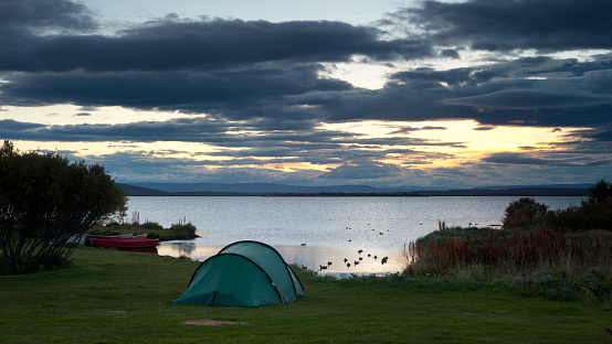 a green tent and red boats during sunset over lake myvatn on iceland