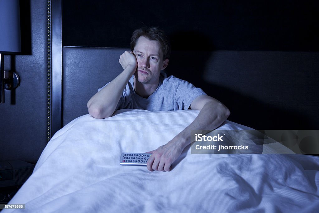 Up All Night Photo of a man sitting in his bed, watching late night television with remote control in hand. Watching TV Stock Photo