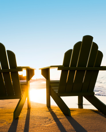 Two beach chairs on a beach facing the sunlight. Vertical shot. 