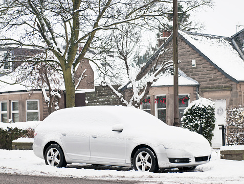 A snow covered car in front of a row of houses on the street in Edinburgh, Scotland.
