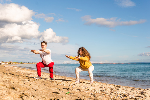 Young couple exercising yoga on the beach at sunrise