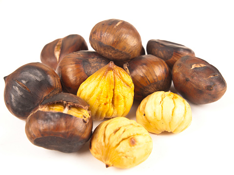 In this image there is a total of twelve roasted chestnuts. There are a total of three that are peeled and nine that are unpeeled and still in their shells. The chestnuts appear to be slightly burnt. The background of this image is static white.