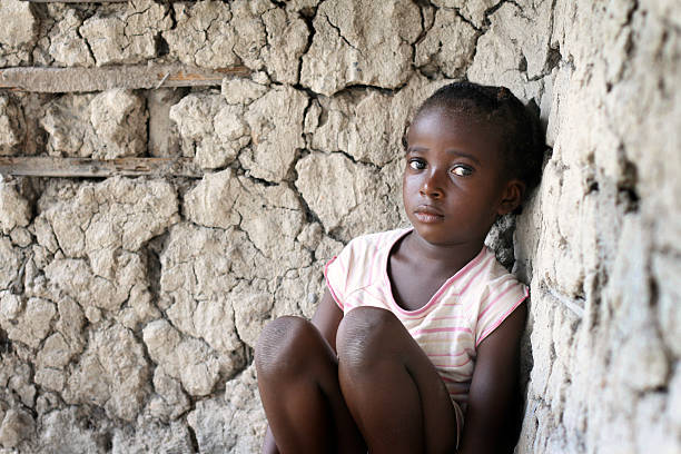 Sad little African girl, sitting against a wall A sad little African girl sitting in the corner of her mud and stick house. sad girl crouching stock pictures, royalty-free photos & images