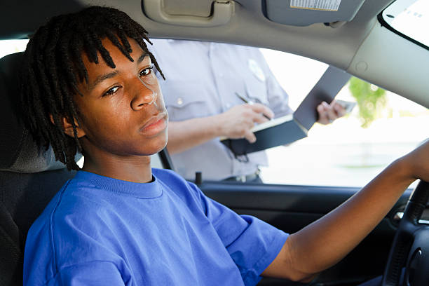 Teenage Boy Receiving a Ticket An unhappy teenage boy receiving a speeding ticket from a police officer. teenager boy driving stock pictures, royalty-free photos & images