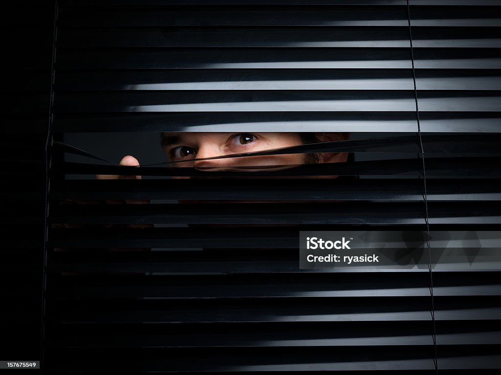 Mysterious Male Peering Out From Opening Behind Blinds A male individual is seen holding down a black blind and is peering out towards the viewer. Canon 5D MarkII. Window Blinds Stock Photo