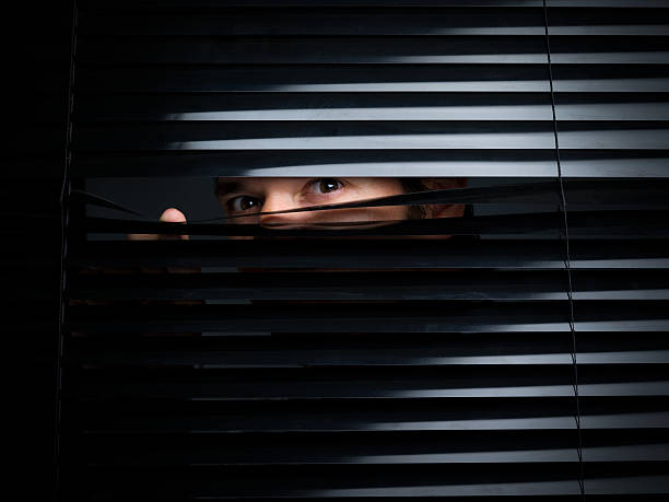 Mysterious Male Peering Out From Opening Behind Blinds A male individual is seen holding down a black blind and is peering out towards the viewer. Canon 5D MarkII. peeking stock pictures, royalty-free photos & images