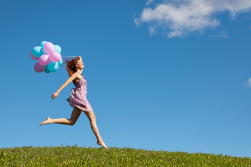 Happy woman jumping on meadow with balloons